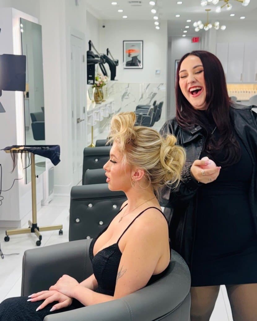 Glam House Salon stylist laughing while finishing a client's high updo