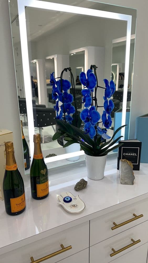 Backlit vanity mirror with blue orchids, Veuve Clicquot champagne, and Chanel book